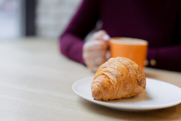 A girl has a croissant for Breakfast in a cafe