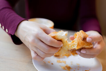 A girl has a croissant for Breakfast in a cafe