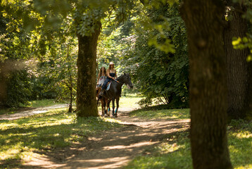 Young girls riding a horse in the city park at summer time.