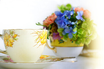 Vintage yellow bone china tea cup and saucer set and flowers arranged in teacup on a bright sunny day. Concept of Mother's Day.