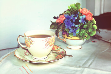 Retro photo of fine china teacup set and flowers on a table. Toned image.
