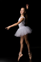 Naklejka premium Cute little girl in a tutu and pointe shoes is dancing in the studio on a black background.