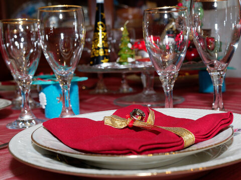 Decorations for a table set for Christmas dinner. A small golden bell placed on a red napkin.