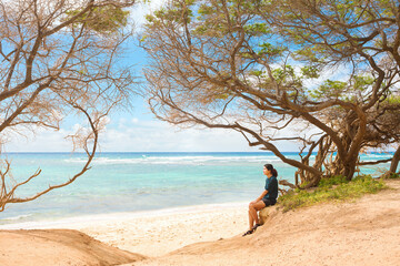 Fototapeta na wymiar One teen girl sitting alone on beach under trees