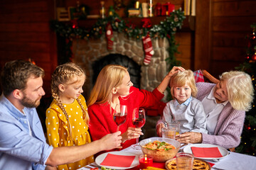 family having fun celebrating Christmas at home, gathered around the table, multi-generation. having Christmas dinner, enjoying winter holiday season at home