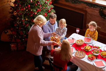 grandmother bring chicken for christmas table, relatives sitting behind it, have meal, at home