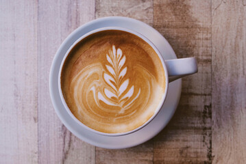 Cup of fresh delicious cappuccino coffee with beautiful latte art on wooden background, close up. From above, copy space.