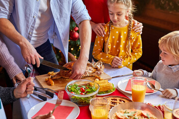 male is carving chicken for christmas or new year, children in anticipation of holiday, having pre-holiday mood