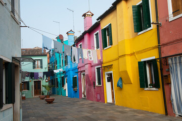Colorful houses on the Italian island Burano, province of Venice, Italy. Multicolored buildings in fog, Italian courtyard with dry laundry outdoor.