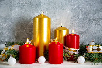 Bunch of red and golden candles burning on wood textured table with traditional christmas wreath decoration, grunged concrete wall background with a lot of copy space for text.