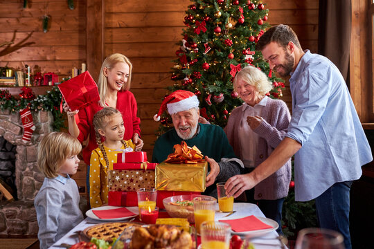 family give christmas gifts to their cute grandfather, children and parents celebrate new year, xmas together
