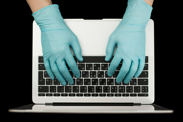 Fototapeta na wymiar Hands in blue protective gloves typing on laptop keyboard. Top view. Coronavirus concept. .