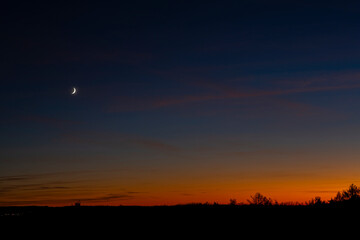 Dusk landscape with the waxing crescent moon over the little town in silhouette.
