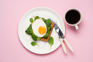 Sunny side up egg with Belgian waffle and spinach. Simple breakfast in plate on pink pastel background