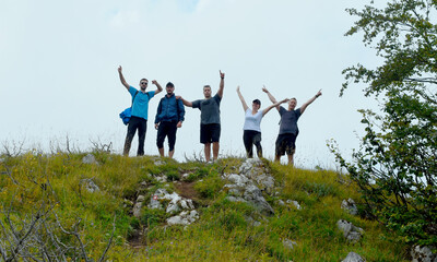 Funf friends on a hiking trip celebrate reaching the summit and have fun posing for photos