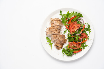 Baked chicken breast with vegetable salad. Chicken fillet with arugula, tomatoes and red bell pepper. White background, top view, copy space