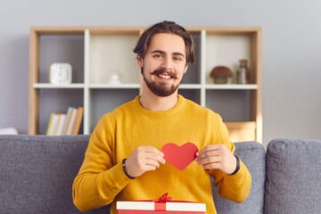 Happy young man smiling showing red heart during online dating and looking at camera