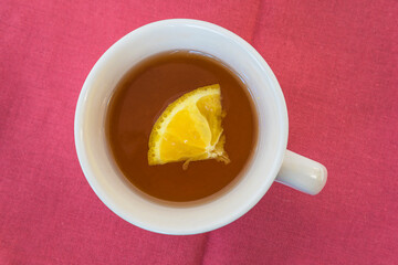 Cup of tea with slice of lemon on red cotton tablecloth. Top view