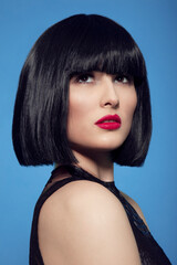 Closeup beauty portrait of a brunette woman in black wig with make up, red lips, over blue background.