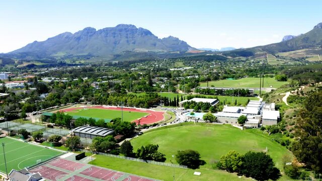 Aerial drone rotating, university college sports athletics stadium, track and field, tennis courts, olympic swimming pool, mountains and trees in background, Stellenbosch, Coetzenburg