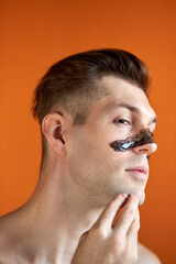 Obraz premium handsome shirtless caucasian guy stand with mask on nose, posing isolated over orange studio background, looking away