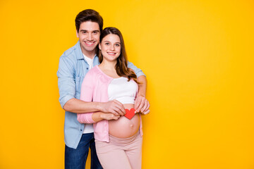 Fototapeta premium Photo of young couple stand hug pregnant woman show paper heart wear casual cloth isolated on yellow background
