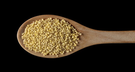 Peeled yellow millet seeds with wooden spoon isolated on black background, top view