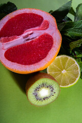 Fruit composition of cut red orange, lime, kiwi and verdure on a light green background