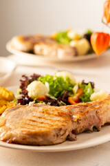 Fried pork entrecote on the bone with stewed pumpkin pieces and salad in a plate close up, green salad with cauliflower and napa cabbage, bell pepper and spices