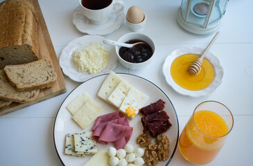 Breakfast plate with various cheeses, bacon, ham and walnuts. With honey, strawberry jam, egg, curd cheese, bread, tea.