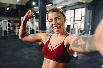 Excited sportswoman showing her bicep and winking while taking selfie