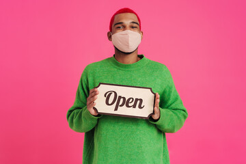 Happy african american guy in face mask holding and showing placard