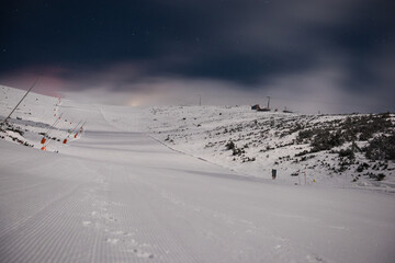 Fresh groomed snow on ski slope at ski resort at cloudy night. Snow groomer tracks on a mountain ski piste.