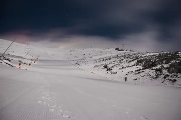 Fotobehang Fresh groomed snow on ski slope at ski resort at cloudy night. Snow groomer tracks on a mountain ski piste. © Filip
