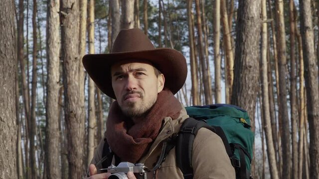 A man in a hat with a backpack takes pictures in the forest. Close-up. Travel concept. 4K