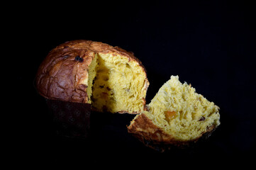 soft and sweet artisanal Italian panettone with a slice cut on a black background and cutting light