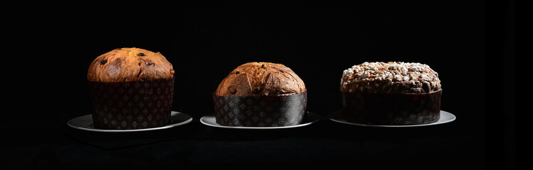 three types of Italian panettone: high, low and with almonds on a black background on a dish with cutting light - obrazy, fototapety, plakaty