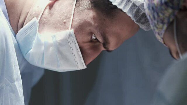 Close up of male surgeon face at work. Action. Side view of a concentrated doctor looking down and wearing protective medical uniform, concept of health.