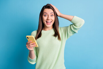 Photo portrait of happy woman touching head with one hand holding phone isolated on pastel blue colored background