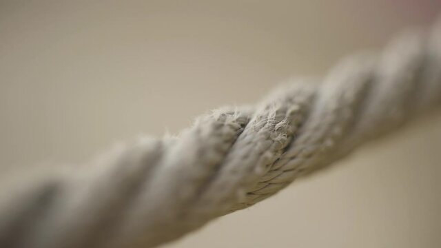 Extreme close up of a rope on blurred beige background. Action. Macro view of a stretched beige rope with a camera focus sliding slowly along the rope.