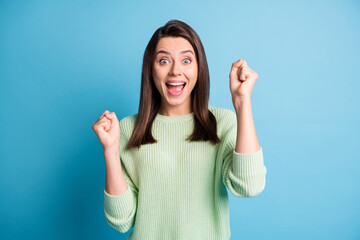 Photo of excited cute lady raise fists open mouth scream rejoice wear green sweater isolated blue color background