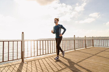 healthy and handsome young male model running on the beach. The man wearing a mask is running by the sea in sportswear. Healthy man who does sports outside with his mask due to corona virus measures.