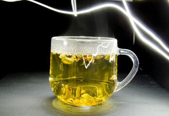 Mug with tea and light stripes on a dark background. Glass mug and green tea