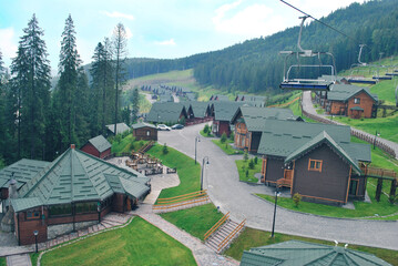 Summer landscape with wooden cottages, ski lift and forested mountains in Carpathians at sunset,...