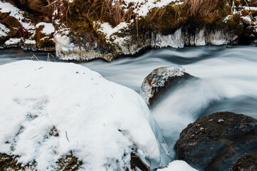 Flow of the river in frozen landscape. Frozen rocks in frozen river.