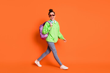 Full length photo portrait of cool schoolgirl walking isolated on vivid orange colored background