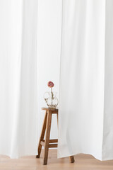 Dry peony flower in a glass jug on a wooden stool in a white room