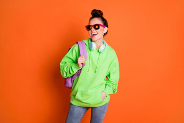 Photo of modern young lady dressed green sweatshirt backpack eyewear looking empty space isolated bright orange color background