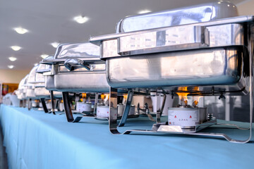 Flames from an alcohol burner under a brilliant stainless steel food warmer. Traveling hot meals during the conference. Kitchen equipment of the restaurant.