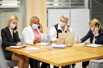 team of mixed race colleagues talking on phone in the office, everyone in medical protective masks coworking during pandemic